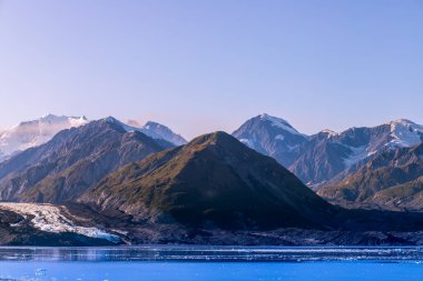 Buzul Körfezi Ulusal Parkı, Yolcu gemisinden karlı dağların manzarası. Güneşli hava, eriyen buzullar, deniz, karlı uçurumlar ve tepeler, açık mavi bir gökyüzü. Küresel ısınma kavramı. Alaska