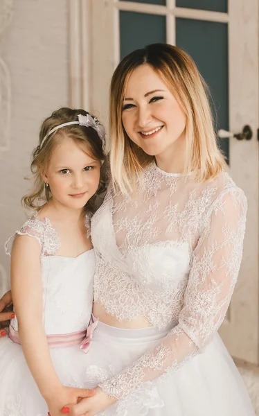 Mother and daughter like brides in white dress huging.