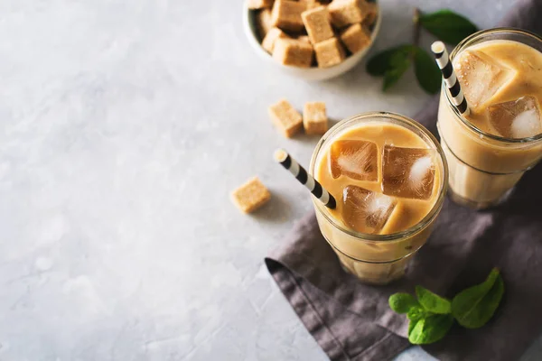 Iced coffee in tall glasses with cream and pieces of sugar, mint