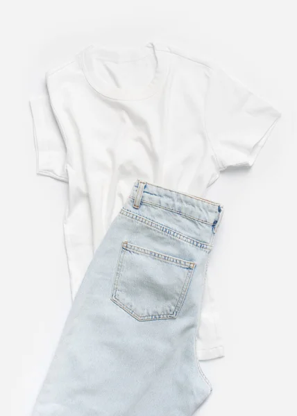 Fashion female clothes on white background. Basic T shirt and denim jeans.  Flat lay, top view.