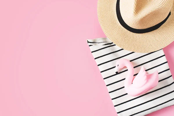 Vacation fashion flat lay with striped t shirt, hat and mini flamingo pastel pink background. Top view