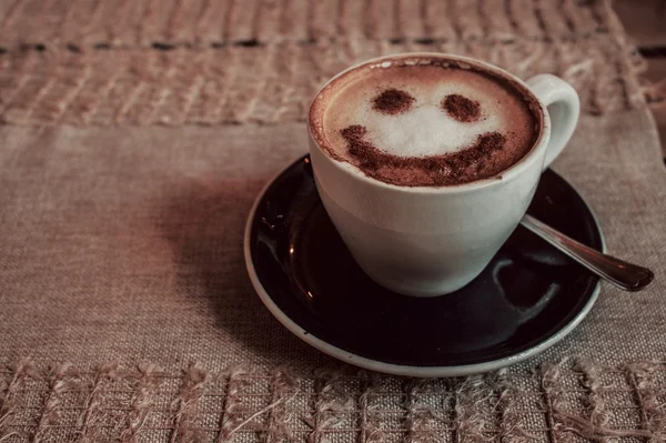 Фото чашки кави капучино на блюдці з принтом посмішка на піні — стокове фото