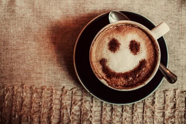 Фото чашки кофе капучино на тарелке с отпечатком улыбки на пене с ложкой на салфетке — стоковое фото