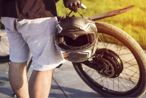 Jovem motociclista com capacete protetor na mão de pé perto da bicicleta elétrica — Fotografia de Stock