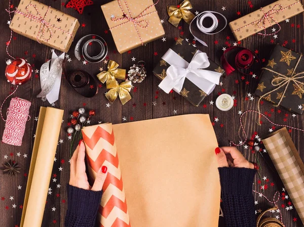 Woman hand unfolding roll of wrapping kraft paper for packing christmas gift box