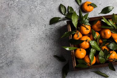 Açık renkli ahşap kutusunda yeşil yaprakları ile mandalina