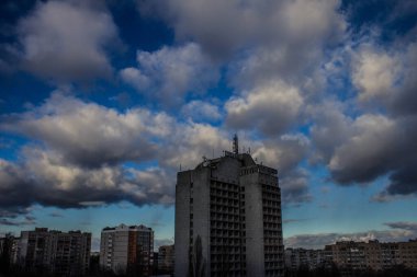 Yüksek binaları olan gri bir şehir. Parlak gökyüzü bulutlarla kaplı..