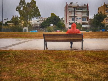 Yağmurlu bir günde dramatik gökyüzü karşı bir parkta bir bankta oturan kırmızı ceket yabancıyla.