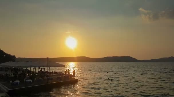 Pessoas silhuetas contra o sol desfrutar de suas férias de verão em Pylos, na Grécia . — Vídeo de Stock