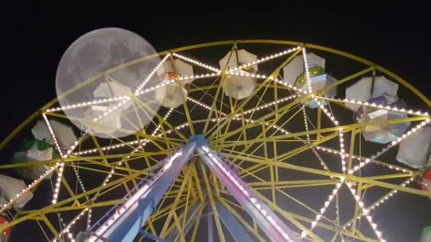 Luna park big wheel met mensen tegen de volle maan. Een surrealistisch uitzicht. — Stockvideo