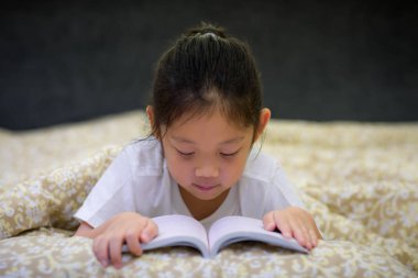 Asyalı çocuk okuma kitabı yatakta