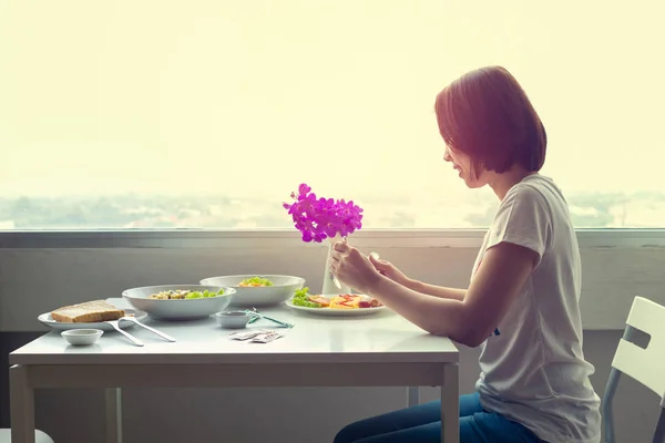Junge Frau sitzt in einem Raum am Tisch und isst allein zu Abend. — Stockfoto