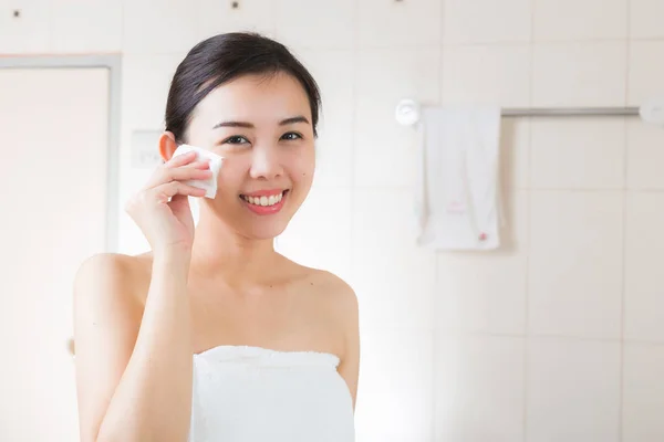 Beautiful woman removing makeup from her face in bathroom.