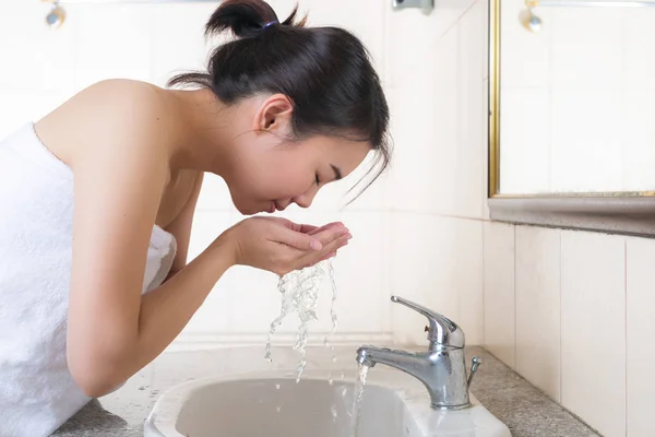Young female washing her face in bathroom.