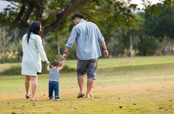 Familia feliz de tres personas caminando por la hierba en el parque . — Foto de Stock