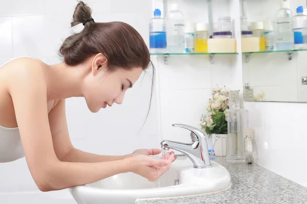 Mulher lavando seu rosto com água acima pia do banheiro . — Fotografia de Stock