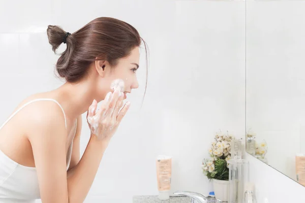 Mujer feliz limpia la piel con espuma en el baño . — Foto de Stock