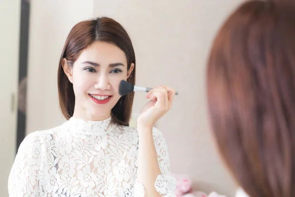 Mujer asiática poniendo maquillaje en casa usando un cepillo de contorno para appl —  Fotos de Stock