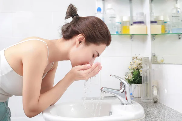 Frau wäscht ihr Gesicht mit Wasser über Waschbecken im Badezimmer. — Stockfoto