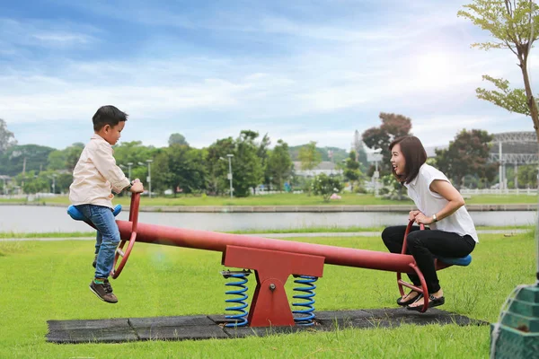 Mãe com filho brincando de baloiço no parque . — Fotografia de Stock