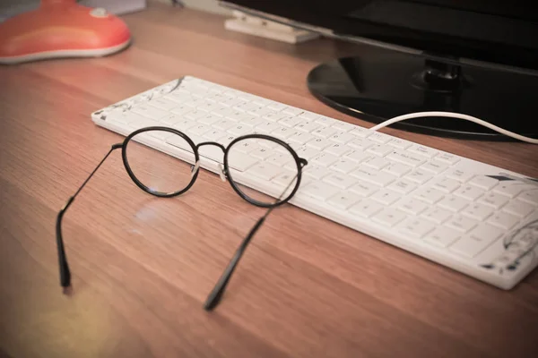 Brille und Tastatur abends auf Holztisch, Nahaufnahme — Stockfoto