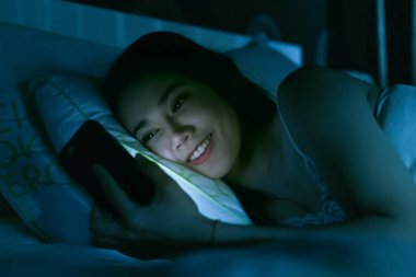 Asyalı kadın yatakta geç gece manifatura cep telefonu lastik kullanarak