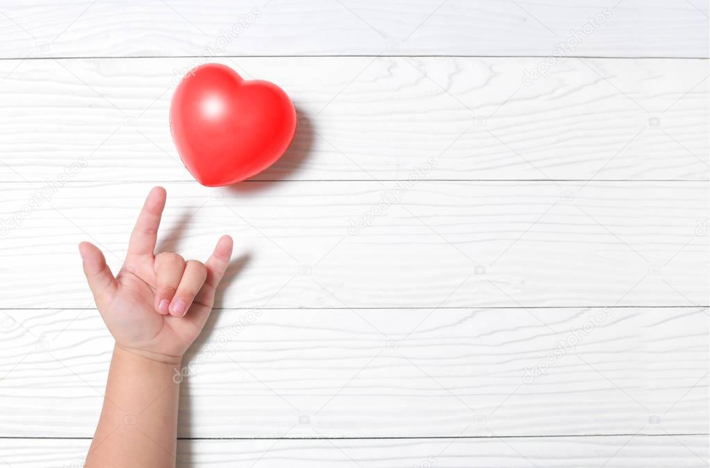 Hand kid supporting love symbol with heart on wooden background.