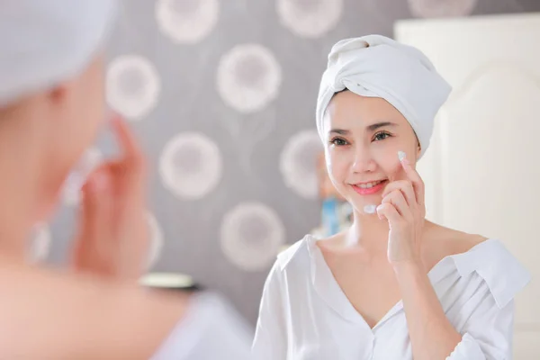 Mujer asiática joven que aplica fundación o crema hidratante en su cara —  Fotos de Stock