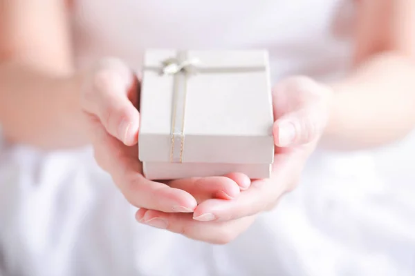 Крупним планом жіночі руки тримають невеликий подарунок, загорнутий стрічкою — стокове фото