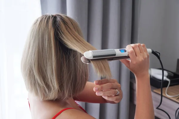 Primer plano de un peluquero alisando el cabello dorado con plancha para el cabello —  Fotos de Stock