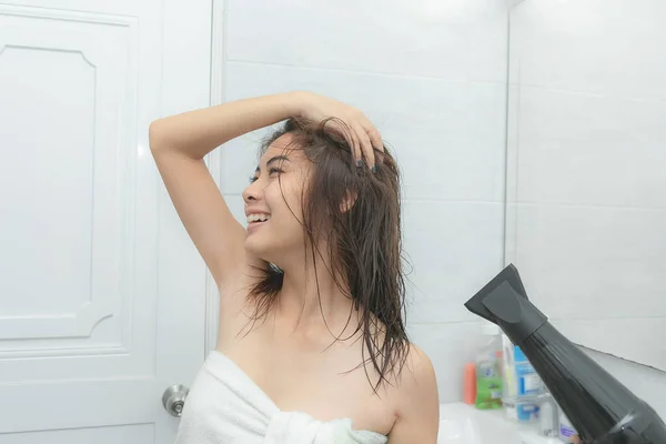 Schöne junge Frau im Badetuch benutzt einen Fön. — Stockfoto