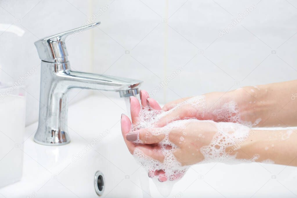 Washing hands with soap under the faucet with water.