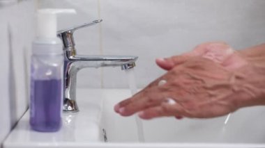 Yaşlı adam musluğun altında sabun ve ellerini yıkıyor. Hijyen konsepti el detayı.