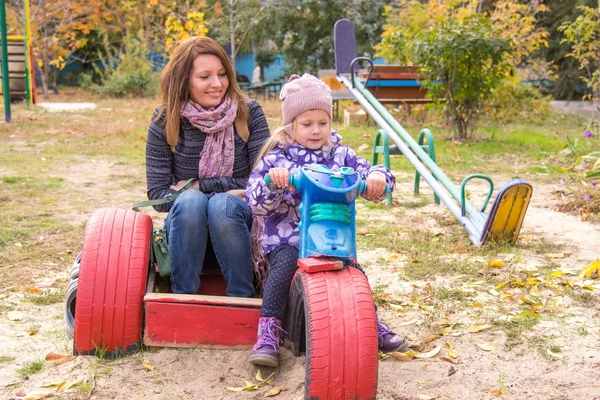 Little girl with her mother sitting at the children's home-made motorcycle in the yard — Stock fotografie