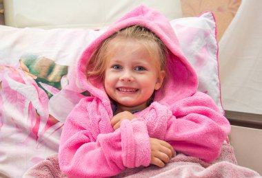 Yatakta sıcak Bornozlu şaşkın küçük kız kameraya doğru görünüyor