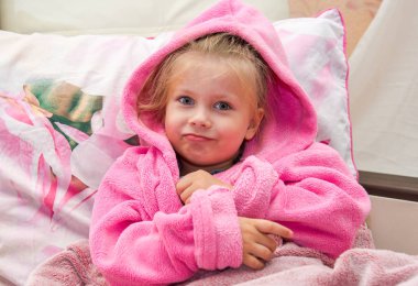 Yatakta sıcak Bornozlu şaşkın küçük kız kameraya doğru görünüyor