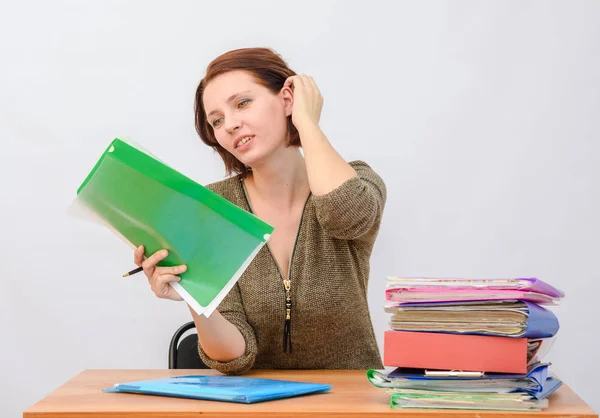 Girl thoughtfully office employee holds documents in a folder and removes hair at the table