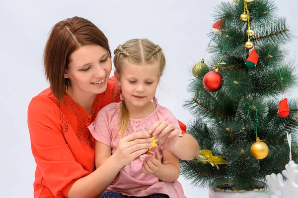 Mãe com uma pequena filha estão preparando uma estrela de ouro e decorar a árvore de Natal — Fotografia de Stock