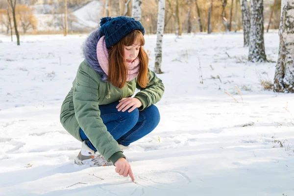 Mladá dívka píše na prst na sněhu v zimě parku — Stock fotografie