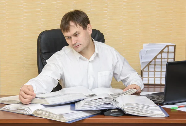 O homem no escritório na mesa olhando para documentos em pastas — Fotografia de Stock