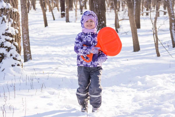 Malý devochkaidet na sněhu s deskou jezdit na kopce a smích — Stock fotografie