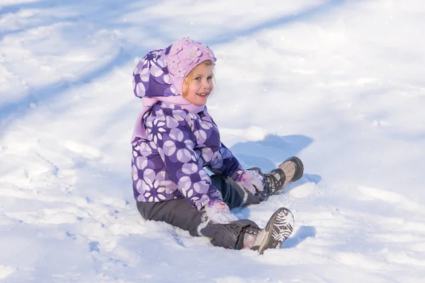 Liten flicka sitter på snön och skrattar — Stockfoto