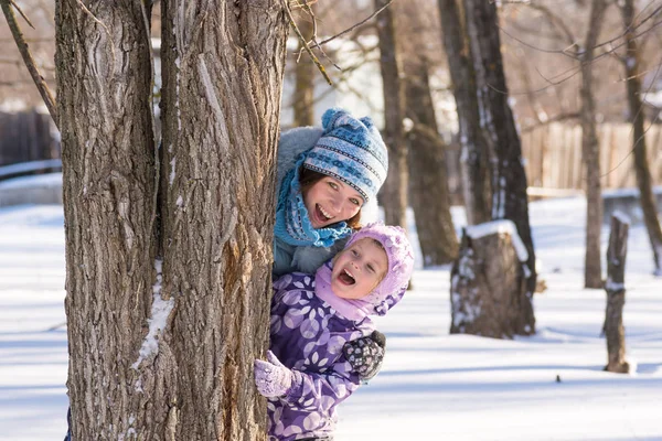 Maminka s malou dcerou vykukoval za strom v zimě lese — Stock fotografie