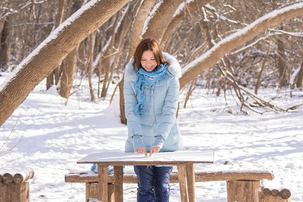 Mladá dívka čerpá na dřevěný stůl pokrytý sněhem v zimě lese — Stock fotografie