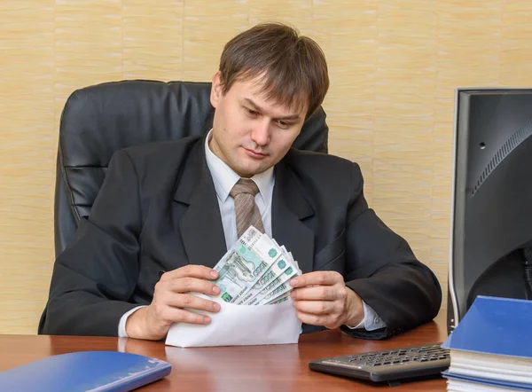 Der Mann im Büro betrachtet das Geld in einem Umschlag — Stockfoto