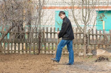 Bir adam bir ülke sitesinde bir kürekle ayakta bir toprak parçası kazmak