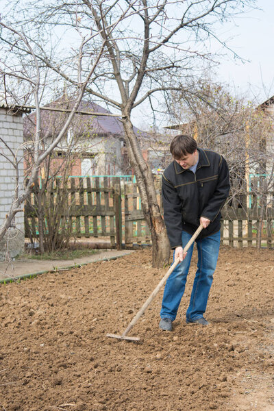 A man near her house loosens rake to dig up a piece of land