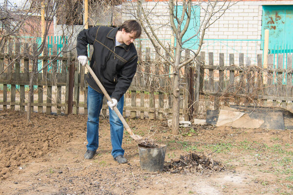 A man on a country site collects the garbage in a bucket
