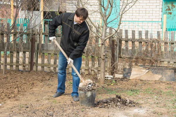 Un hombre en un sitio de campo recoge la basura en un cubo — Foto de Stock