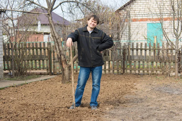 A man standing on a country site with a rake to dig up a piece of land Stock Photo
